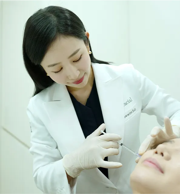 누워 있는 환자의 얼굴에 주사 시술을 하는 대표원장