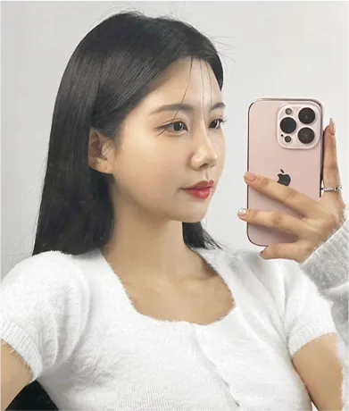 리프팅 후기 인물 사진 — 거울 앞에서 휴대폰으로 찍은 여성 상반신